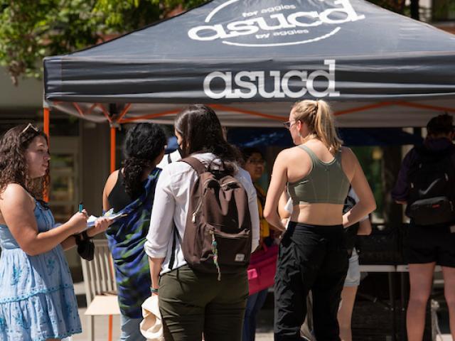 Students in line for food distribution, with an ASUCD black tent in the background.